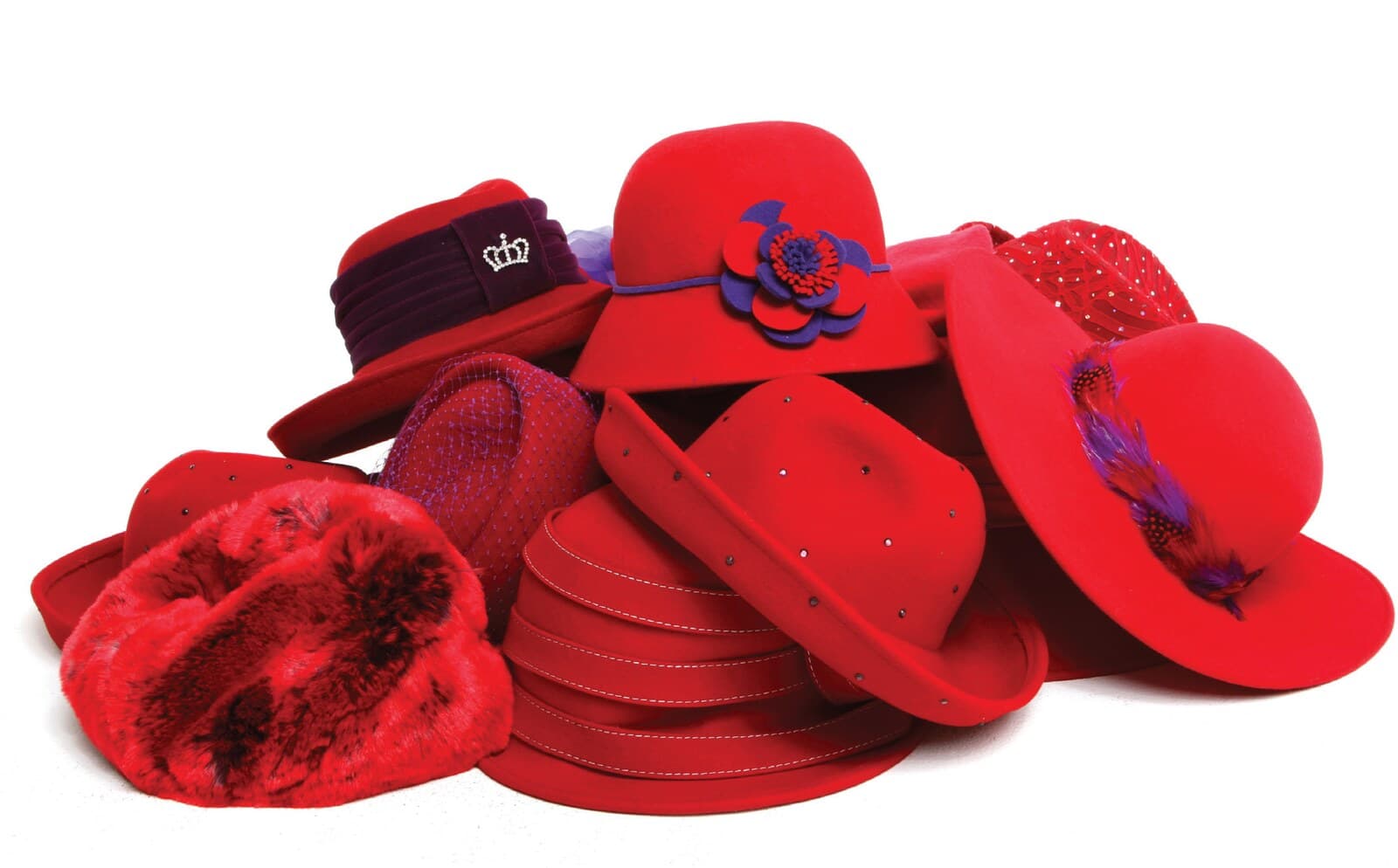 A pile of red hats in felt, velvet and faux fur, trimmed with purple flowers and feathers.